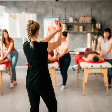 A massage therapy class with instructor demonstrating hand techniques.