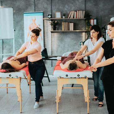 Two therapists giving arm massages to clients on massage tables in a serene room.