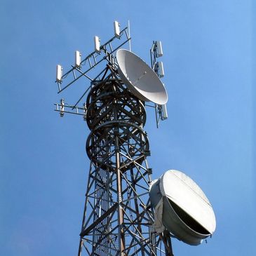 A tall communication tower with multiple antennas and satellite dishes against a blue sky.