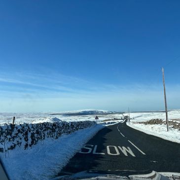 Snow-covered road with clear blue sky and 'SLOW' painted on the asphalt.