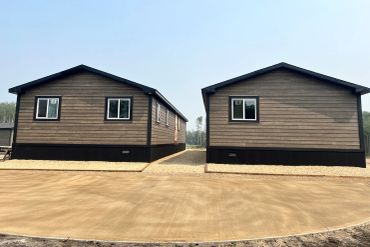 Two modern, identical wooden houses with black bases under a clear sky.