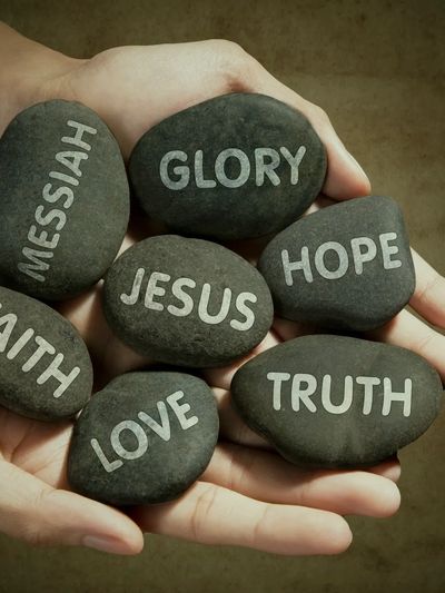 Hands holding stones with words representing Christian faith and values.