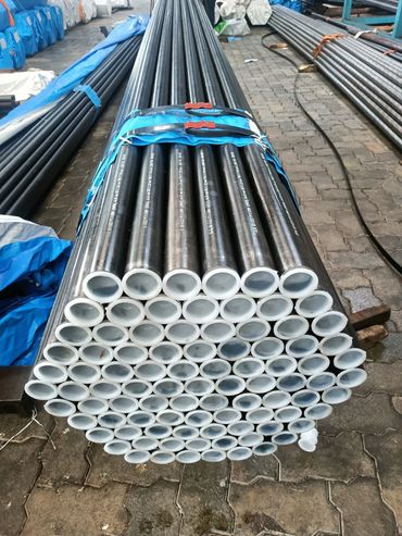 Stack of bundled black metal pipes with white inner linings in a warehouse.