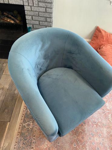 A blue velvet armchair on a patterned rug near a brick fireplace.
