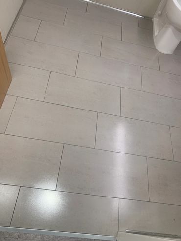 Clean beige rectangular floor tiles in a bathroom with a white toilet.