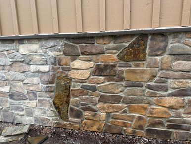 A stone wall with variously shaped stones beneath wooden siding.