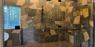 Spacious rustic stone-tiled shower with glass doors and black fixtures.