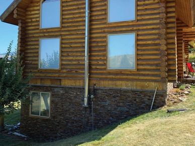 Log cabin with large windows on a grassy hill under clear blue sky.