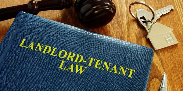 A book on landlord-tenant law with a gavel, house key, and pen on a wooden surface.