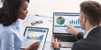 Two professionals analyzing financial data on a laptop and tablet.