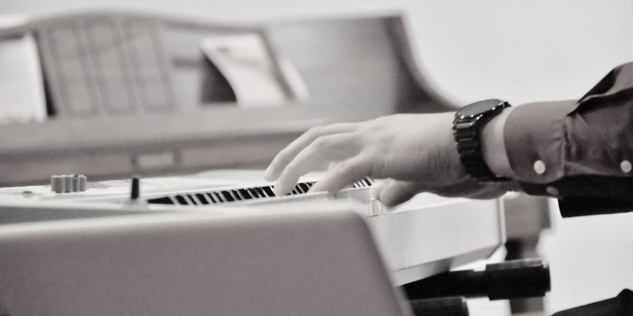 Person playing a keyboard piano with focus on their hand and wristwatch.