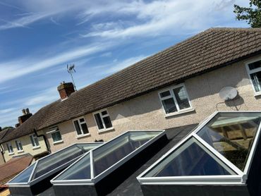 Row of skylights on a flat roof under a blue sky with clouds.
