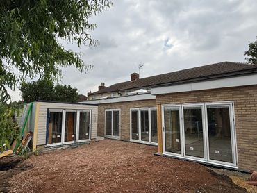 Newly constructed modern house extension with large glass doors and unfinished yard.