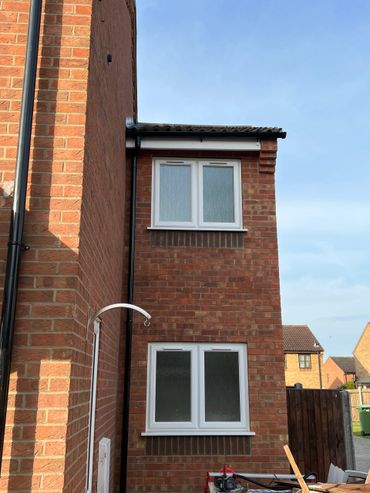 Two-story brick house with white-framed windows and a clear blue sky.