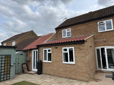 Brick house with red tiled roof and garden sheds under cloudy sky.