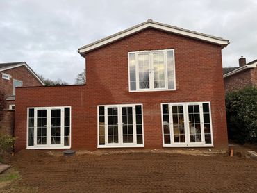 Newly constructed brick house extension with large white-framed windows and doors.