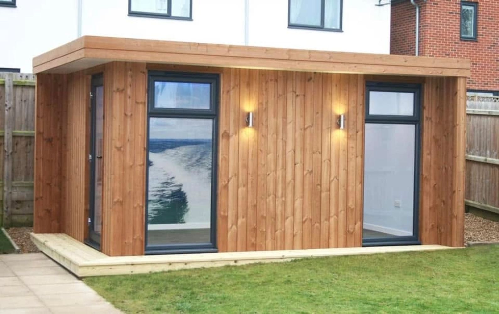 Modern wooden garden office with large windows and exterior lights.