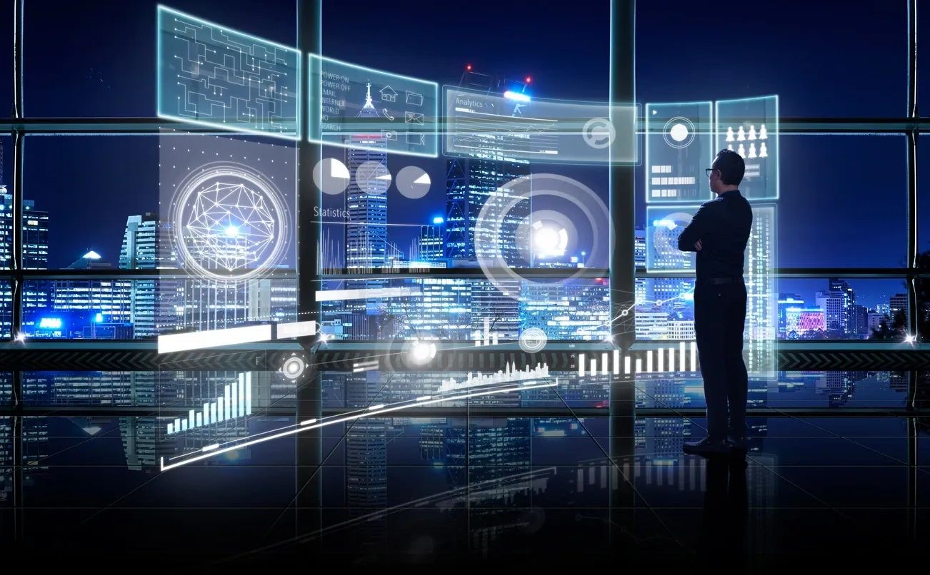 A person stands in a high-tech room, viewing holographic data and city lights through large windows.