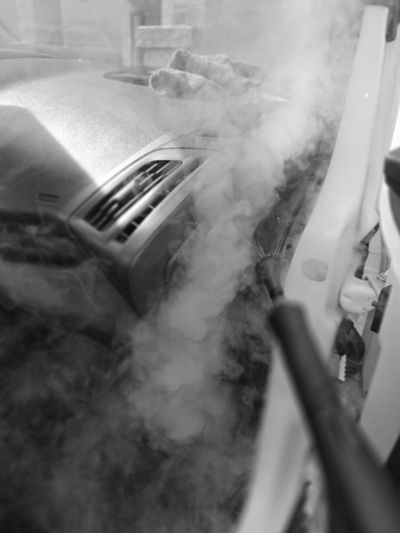 Steam cleaning a car's interior dashboard and air vents.