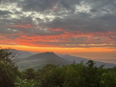 Sunset over lush mountains with a reflective water surface in the foreground.