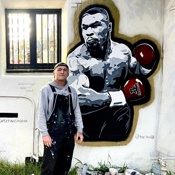 Artist posing next to a mural of a boxer on a wall.