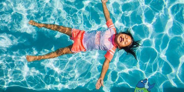 A joyful child floats on water in a swimming pool under bright sunlight.