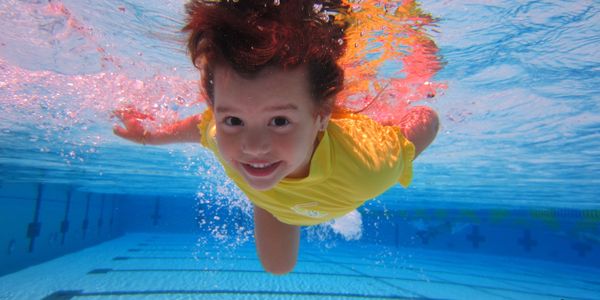 Child swimming underwater in a pool wearing a yellow shirt.