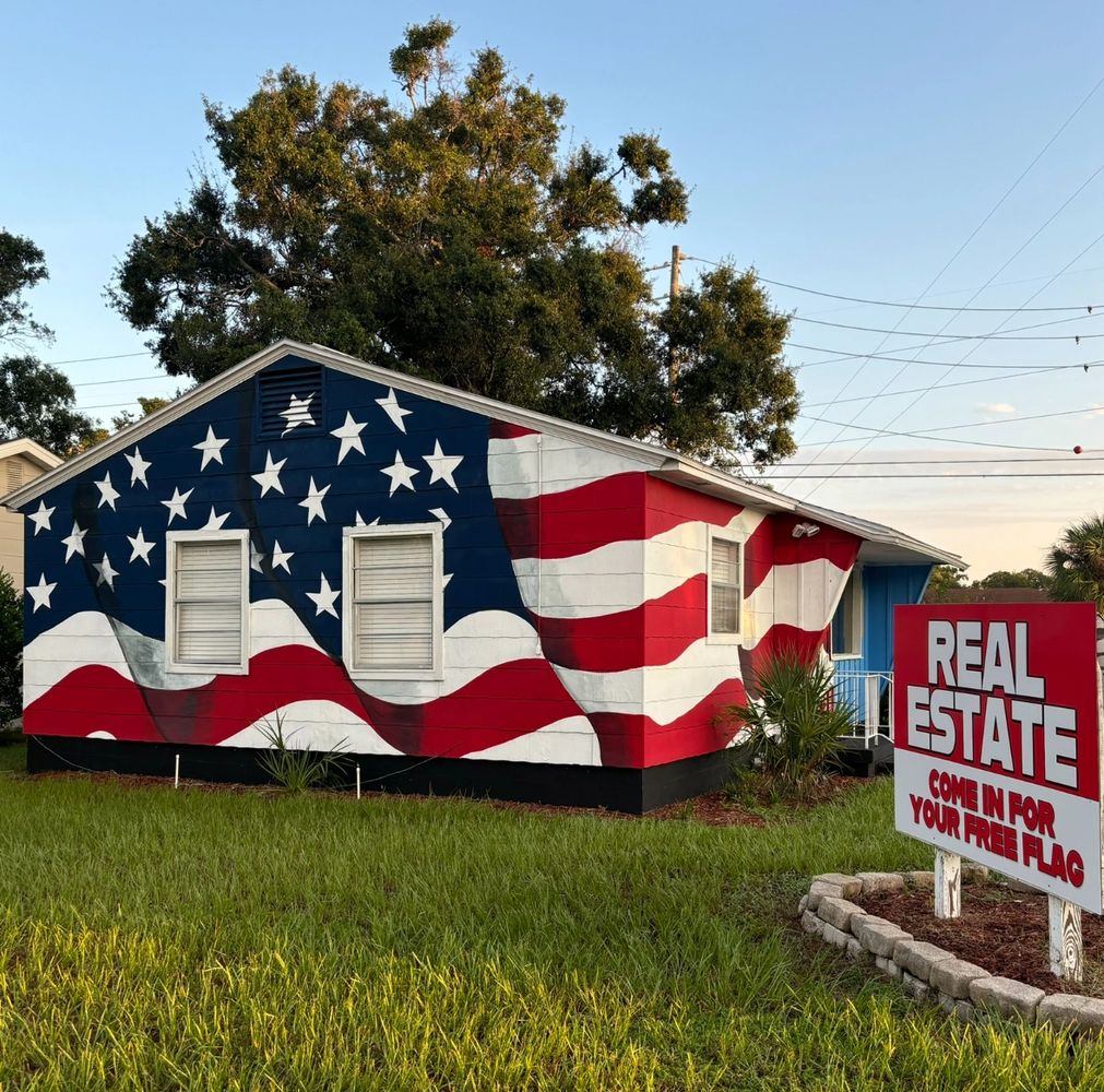 House painted with a large American flag and a real estate sign offering free flags.