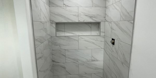 Custom marble-look tile shower with recessed storage niche and carefully aligned large-format wall t