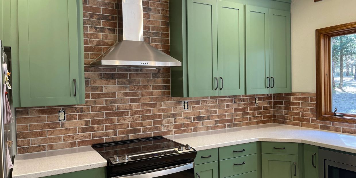 Completed kitchen remodel with sage green cabinets, brick backsplash, white countertops, and stainle