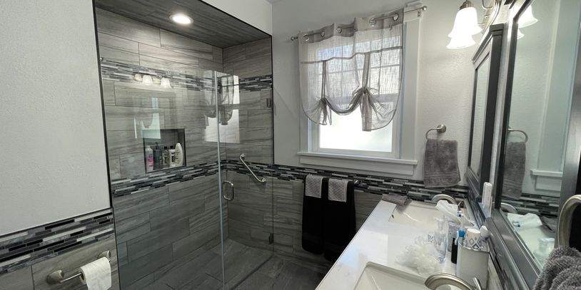 Modern gray tiled bathroom with glass shower and white sink.