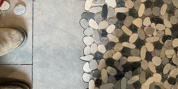 Pebble mosaic tile floor detail beside large-format gray tile, showing precise layout and finish wor