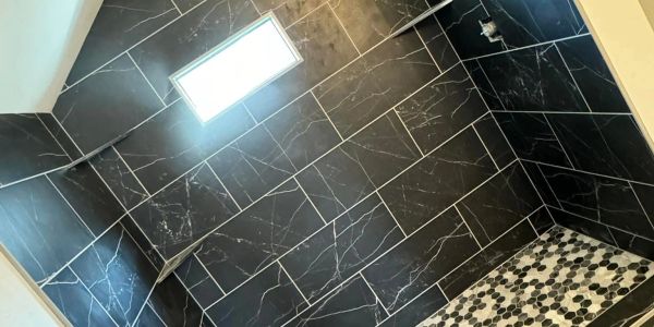 Black large-format tile shower with pebble mosaic floor, recessed niche, and clean grout lines.