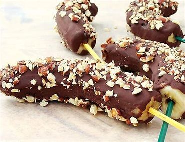 Chocolate-covered bananas sprinkled with nuts on sticks.