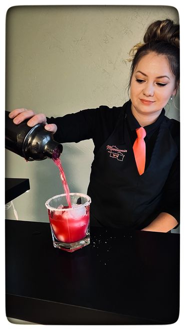 Bartender pouring a red cocktail into a glass with ice and a salted rim.