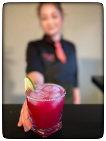 A vibrant pink cocktail with ice and lime, held by a smiling person.