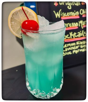 Blue cocktail with ice, cherry, and lemon slice garnish.
