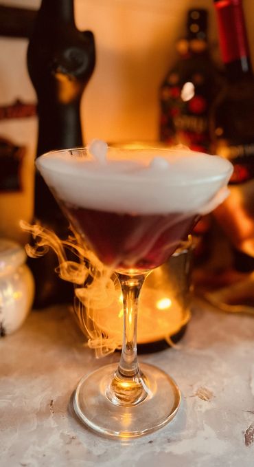 Elegant cocktail with frothy top and smoky effect in a dimly lit setting.