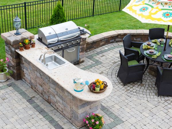 an aerial shot of a masonry stone outdoor kitchen with grill, built in sink, and seating area
