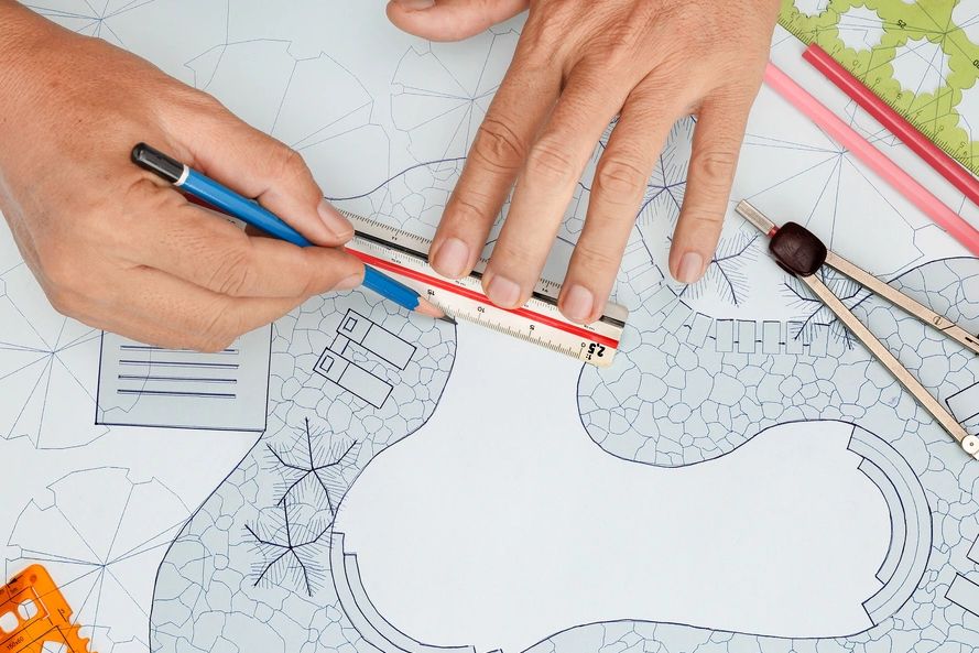 a pair of hands drawing a blueprint design of a backyard swimming pool