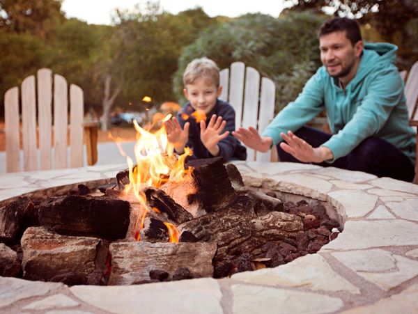 a man and boy warming their hands by a stone outdoor fire pit