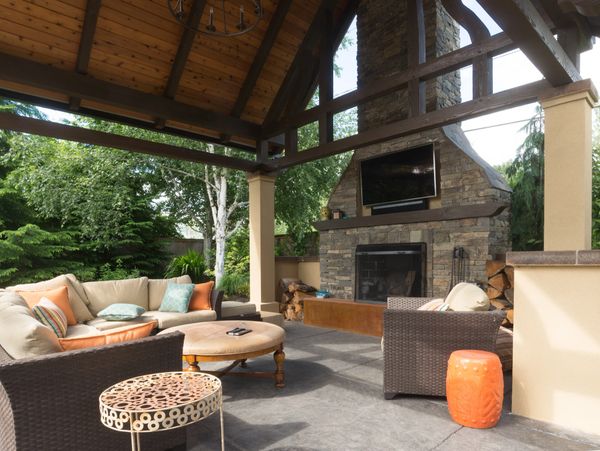 an outdoor living room with a vaulted wooden ceiling and stone masonry fireplace with TV and seating