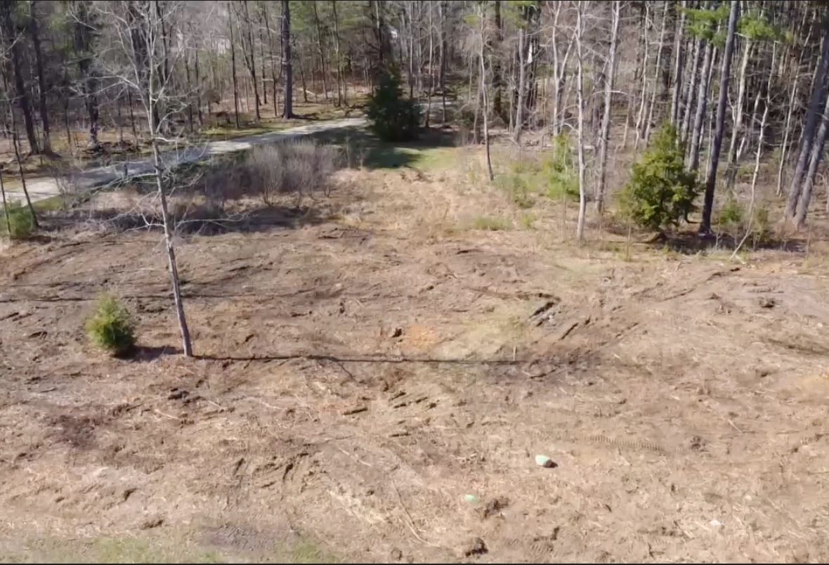 Cleared land area with scattered trees and visible tire tracks.