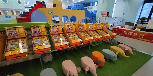 Row of vintage pachinko machines with colorful animal stools in front.