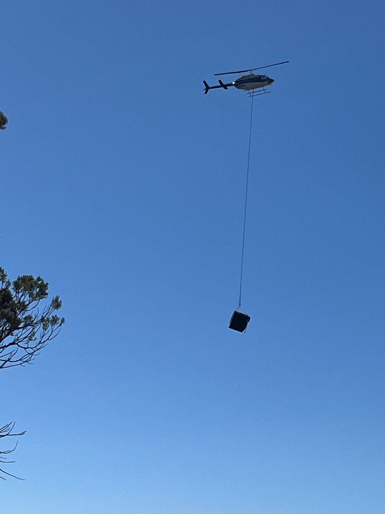 Helicopter carrying a heavy load under a clear blue sky.