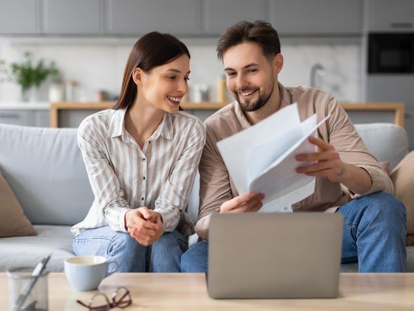 A smiling couple reviewing documents while sitting on a couch.