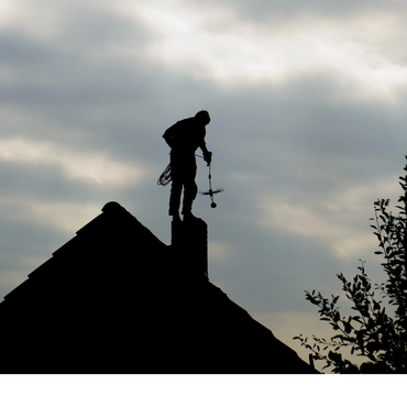 Silhouette of a person working on a chimney at dusk.