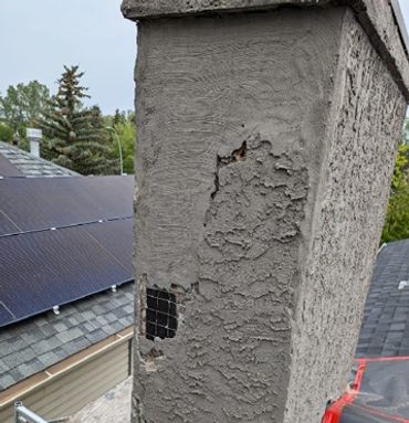 A chimney with damaged cement and exposed wire mesh on a rooftop.