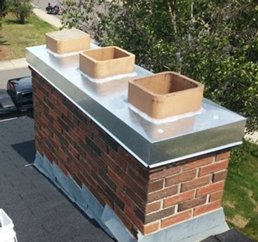 A brick chimney with three rectangular flues on a rooftop.