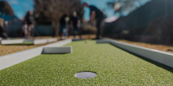 Close-up of a mini golf hole with players in the background.